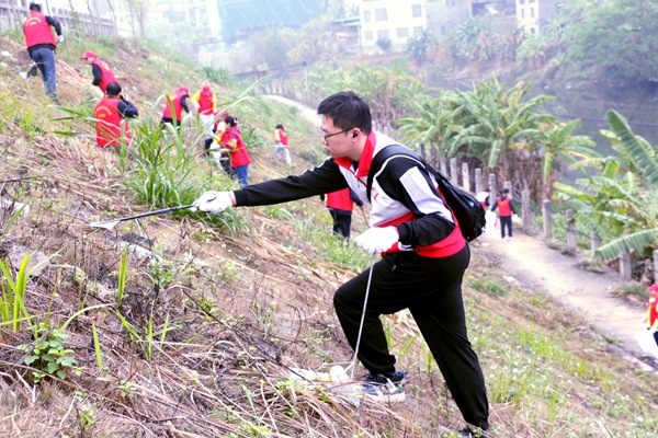 身穿红色马甲的青年党员志愿者，沿着河岸捡拾垃圾。覃嘉川摄影